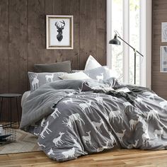 a bed with grey and white deer print on it, next to a wooden wall