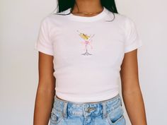 Martini Baby Tee   Women's T-Shirt | Girly Aesthetic | Y2K Trendy Shirt 🌟SHIRT This is a Bella+Canvas baby tee - the material is very soft and very high quality. 🌟SIZING Please find the size chart in listing photo before purchasing. We recommended measuring a t-shirt you already own to get the best fitting t-shirt. 💖CARE/ WASH Machine wash: warm (max 40C or 105F); Non-chlorine: bleach as needed Tumble dry: medium heat; Iron, steam or dry: low heat; Do not dry clean. ✨SHIPPING Your items usually will ship in 2-7 business days. Products shipped from US.  Thanks for shopping small.  Please let me know if you need any custom designs or bulk orders that is not listed, I'll happily custom-make it for you! ♡ Pink Fitted Graphic Tee, Fitted Pink Graphic Tee Shirt, Cute Fitted Summer T-shirt, Cute Fitted Cotton Shirt, Cute Fitted Pink T-shirt, Pink Fitted Cute T-shirt, Fitted Pink Cute T-shirt, Cute Fitted Shirt With Graphic Print, Fitted Cute Shirt With Graphic Print