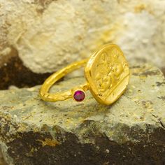 Roman Greek Art signed coin ring made 24k gold plated 925 sterling silver and used Reproduction Bronze Coin with Red Diamond Cut Cubic Zirconia Stones on each side.Handcrafted hammered full round ring band size measures 2mm in width and 24k gold plated bronze coin 14x16.5 mm.Metal : 925 Sterling SilverBand Width : 2 mmGem Stone : Red Diamond Cut Cubic ZirconiaGem Color : Green,Navy Blue,Purple,Blue,White,Red(The color you want is made for free).Gem Size : 3 mmCoin : Reproduction Bronze CoinCoin Engraved Gold Ruby Ring Gift, Gold Byzantine Ruby Ring For Gift, 22k Gold Ruby Ring For Gift, Handmade Heirloom Ruby Ring In Gold, 22k Gold Byzantine Style Rings As Gift, Handmade 14k Gold Ruby Ring, Gold Ruby Ring, 14k Gold, Hammered Jewelry, Man Ring