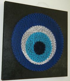 a blue and white eyeball made out of yarn on a black canvas mounted on a wall