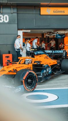 an orange race car is parked in front of a building with people standing around it