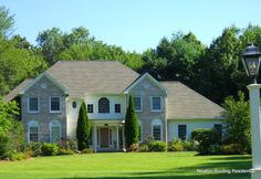 a large white house surrounded by lush green trees and grass with a lamp post in front