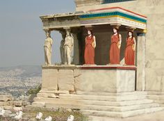 some statues on the side of a building with birds around them in front of it