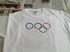 a t - shirt with the olympic rings on it is laying next to news paper