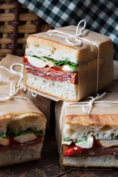 several sandwiches wrapped in brown paper sitting on top of each other, with one sandwich cut in half