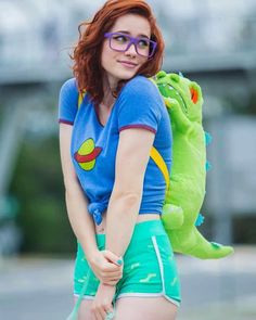 a woman with red hair and glasses carrying a green stuffed animal on her back,