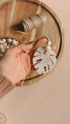 a person is holding something in their hand on a wooden tray with white beads and twine