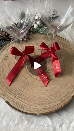 two wine glasses sitting on top of a piece of wood next to pine cones and christmas decorations