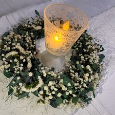 a candle is lit in the middle of a wreath on a table with white lace