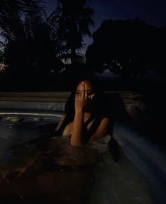 a woman is sitting in the hot tub talking on her cell phone at night time