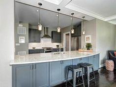 a large kitchen with gray cabinets and marble counter tops, along with bar stools