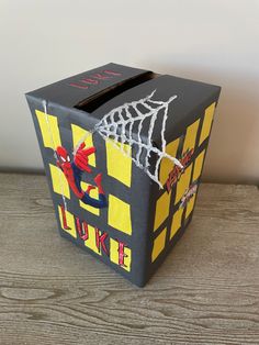 a spiderman themed tissue box sitting on top of a wooden table next to a white wall