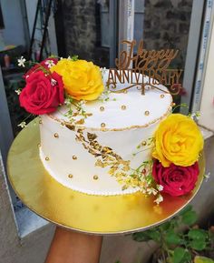 a white cake with yellow and red flowers on top is sitting on a gold platter