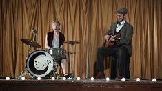 a man and woman are playing instruments in front of a stage with curtains behind them