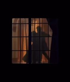 the silhouette of a man standing in front of a window with curtains behind him,