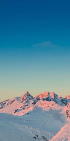 the mountains are covered in snow as the sun sets