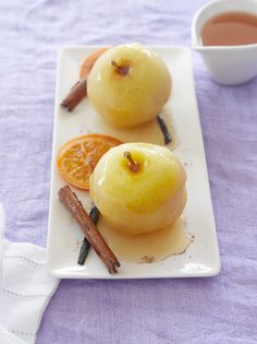 two pieces of fruit on a plate with cinnamon sticks and a cup of tea in the background