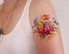 a woman with a flower tattoo on her left arm and right arm is wearing a white tank top