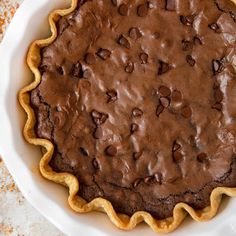 a chocolate pie in a white dish on top of a table with a brownie crust