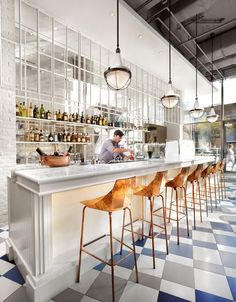 a man sitting at a bar with lots of bottles on the wall behind him and stools in front of it