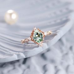 an engagement ring with a green and white stone surrounded by pearls on a wavy background