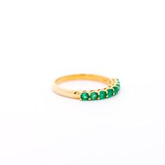 a gold ring with green stones on the inside and outside, set against a white background