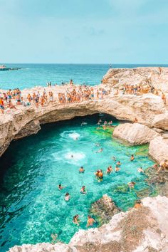 people are swimming in the blue water near an arch shaped rock bridge that stretches into the ocean