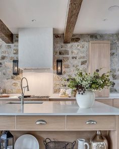 a kitchen with stone walls and white counter tops, an island in the middle is surrounded by pots and pans