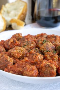 a white bowl filled with meatballs on top of a table next to slices of bread