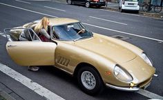 a woman sitting in the driver's seat of a tan sports car on a city street