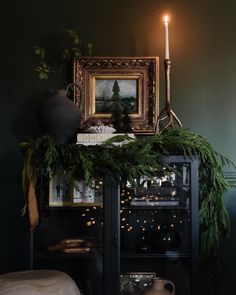 a candle is lit on top of a mantle with greenery and candlesticks