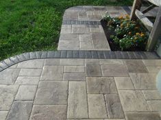 an outdoor patio with brick pavers and flowerbed in the corner, surrounded by grass