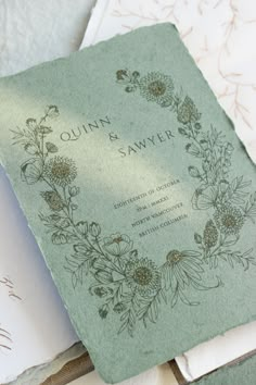 the wedding program is sitting on top of some folded papers with flowers and leaves printed on them