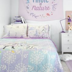 a bed with purple and blue comforter next to a wall hanging on the wall