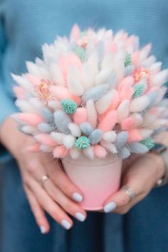 a woman holding a pink and white flower pot filled with fake flowers in her hands