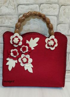 a red handbag with white flowers and wooden handles on a table next to a brick wall