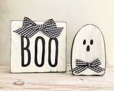 two wooden signs decorated with black and white designs, one has a ghost face and the other has a bow