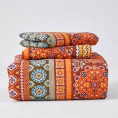 three pillows stacked on top of each other in front of a white background with an orange and blue pattern