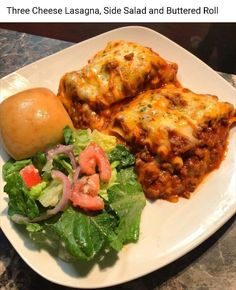 a white plate topped with lasagna, salad and buttered roll