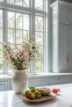 a white vase filled with flowers sitting on top of a counter next to fruit and vegetables