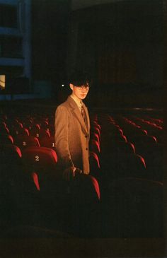 a man in a suit and tie standing next to rows of red seats at an auditorium