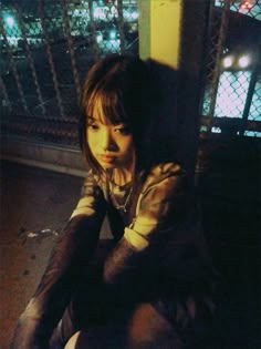 a woman sitting on the ground in front of a fence