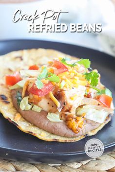 a black plate topped with an enchilada covered in cheese and toppings