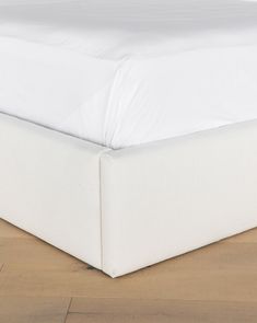 a bed with white sheets on top of it and wood flooring in the background