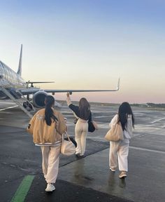 three people walking towards an airplane on the tarmac at sunset or sunrise, with one person in white pants and brown jacket