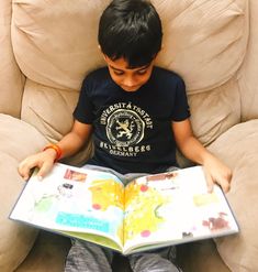 a young boy sitting on a couch reading a book