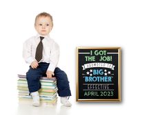 a little boy sitting on top of a pile of books next to a chalkboard