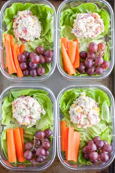 four plastic containers filled with salad and carrots next to grapes on top of lettuce