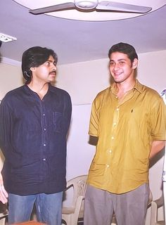 two men standing next to each other in front of a ceiling fan and table with food on it