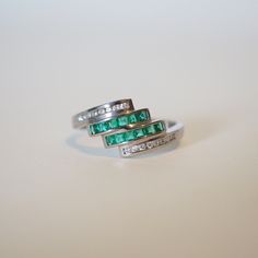 This ring is a beautiful overlapping ring in 18K solid white gold. The ring is decorated by green squared emeralds channeled into 2 lines overlapping one another and round diamond accents to add to the sparkle. It is a fun ring for every day wear no matter the age or gender. This one is however a woman size ring but we can resize for you. Product Details: Metal: 18k Solid Gold Metal Color: White Gold Total weight: 4.00 grams Emerald: Natural, minor clarity enhancement, square cut, 0.40 carats Di Green Multi-stone Emerald Rings, Green Emerald Cut Multi-stone Diamond Ring, Emerald Cut Green Multi-stone Diamond Ring, Emerald Cut Green Diamond Ring With Multi-stone, Fine Jewelry With Channel Set Green Stones, Fine Jewelry Green Channel Set, Fine Green Jewelry With Channel Set, Green Channel Set Fine Jewelry, Luxury Green Channel Set Rings